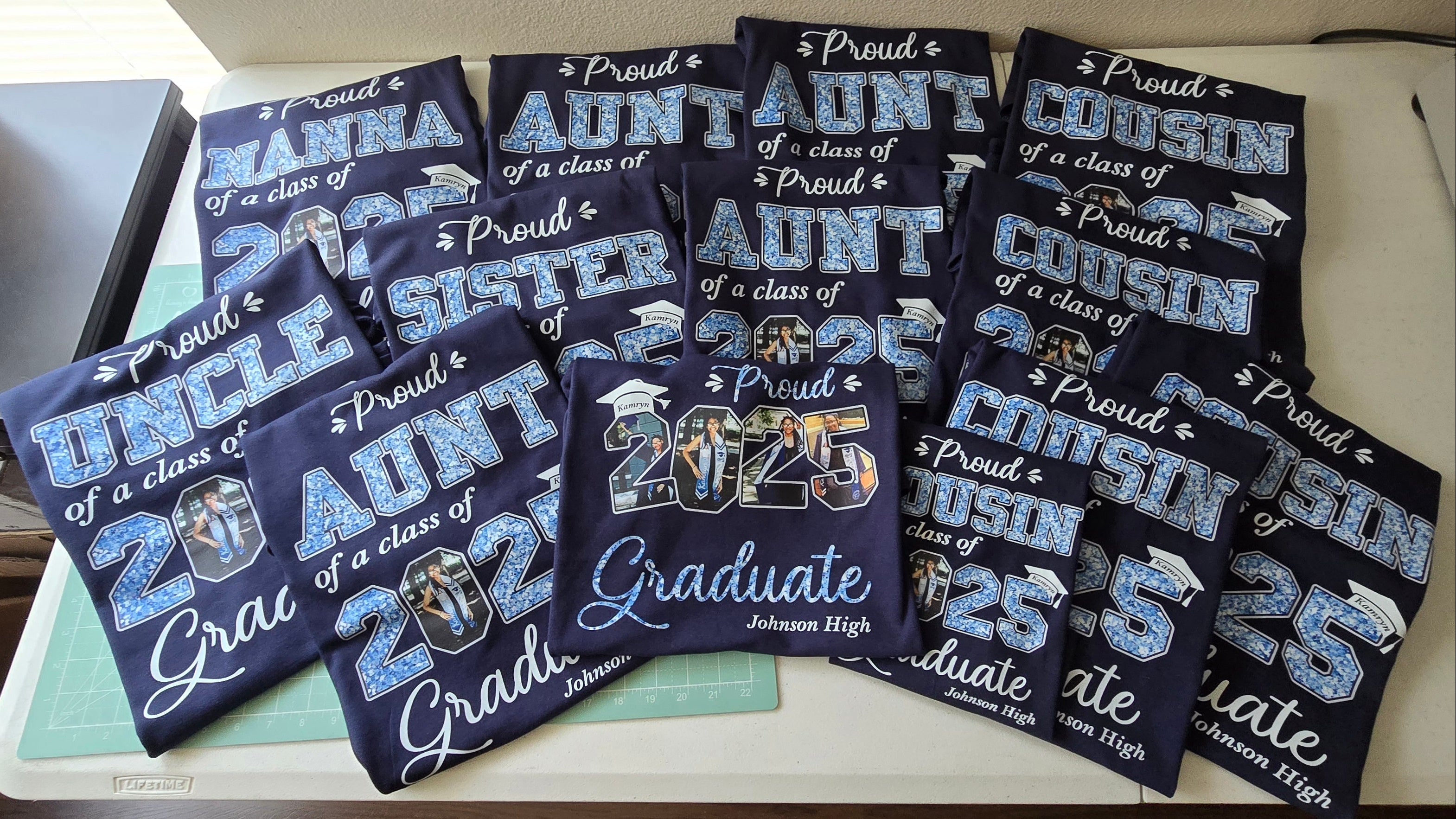 Collection of graduation-themed shirts with text like 'Proud Aunt of a class of 2025' on a white surface.