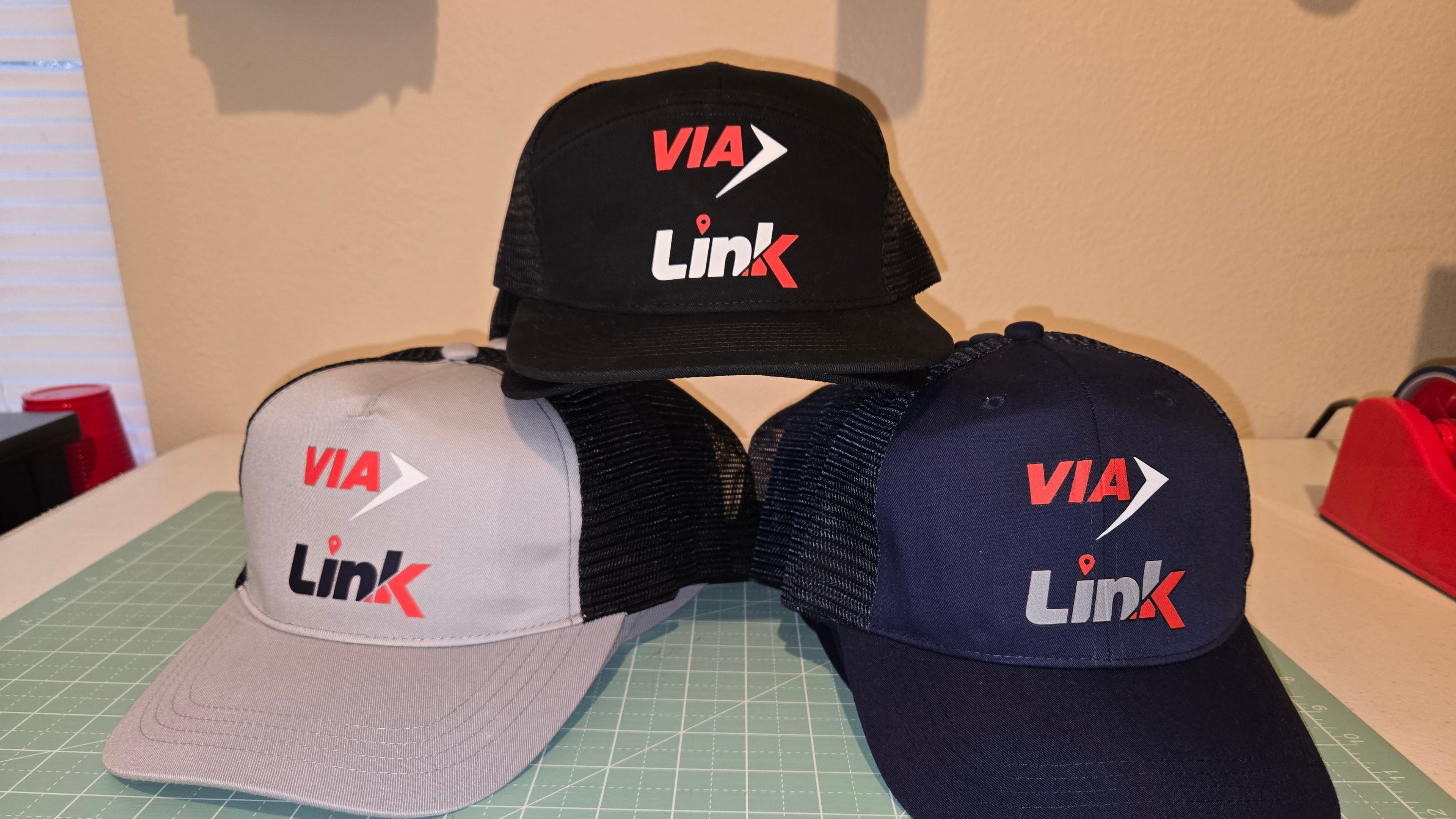 Three caps with 'VIA Link' logo on a cutting mat